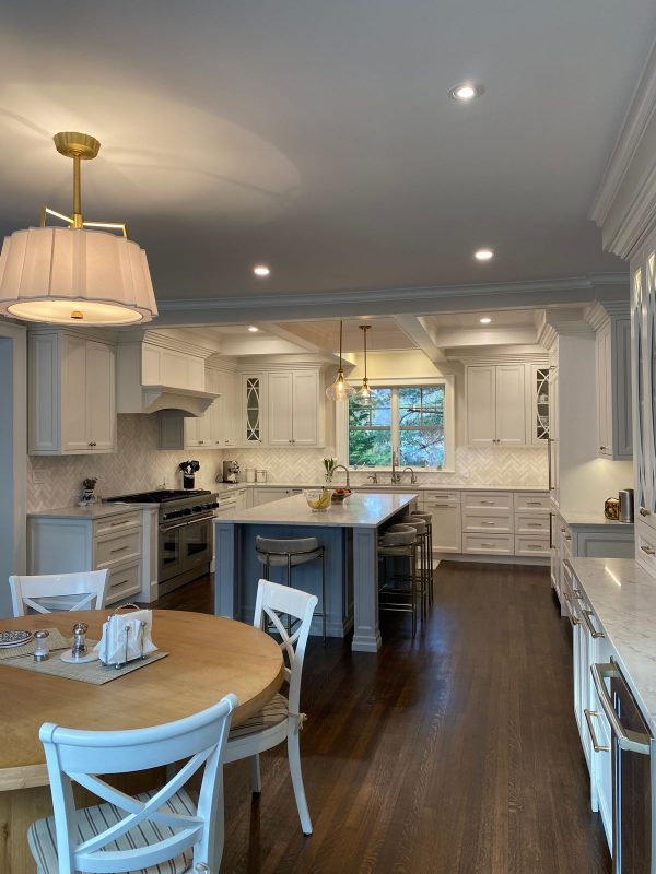 Spacious kitchen with white cabinets, stainless steel appliances, a central island, a round wooden table with chairs in the foreground, and two pendant lights.