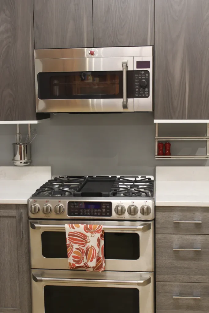 Modern kitchen with stainless steel microwave and gas stove. A towel with orange patterns hangs on the oven handle. Cabinets and countertop surround the appliances.