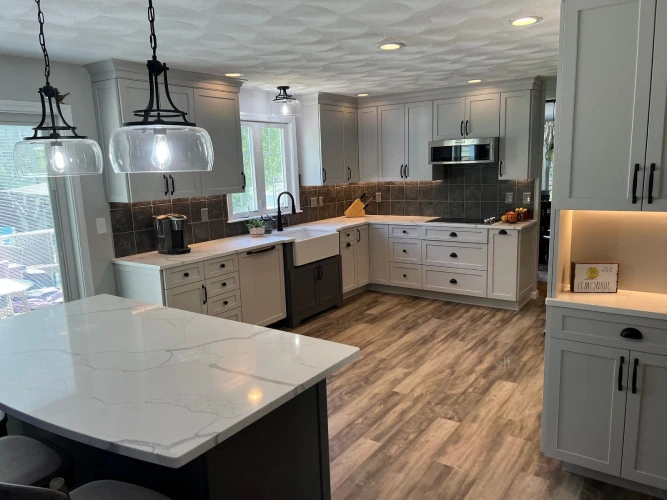 Modern kitchen remodel with gray shaker cabinets, white quartz countertops, and wood-look flooring